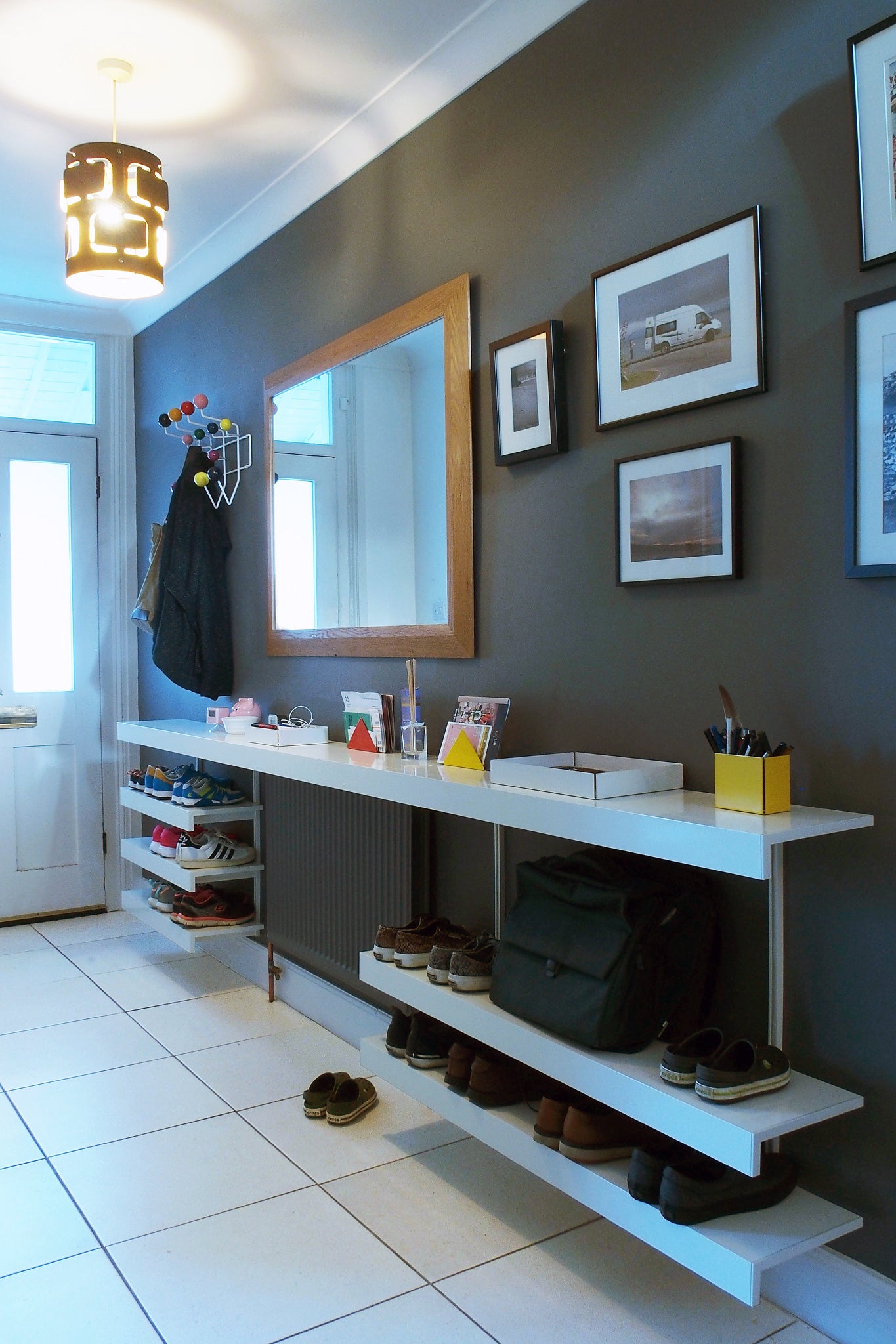 Hallway with modern white long shelving for bags and shoes below mirror