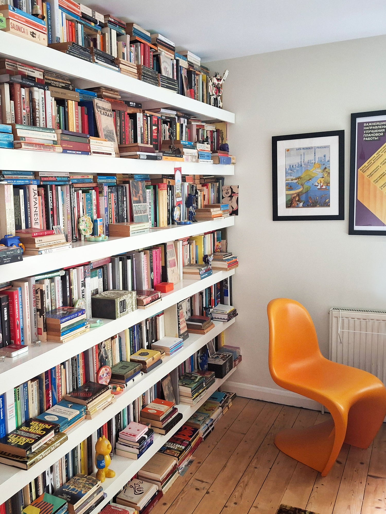 white long book shelving wall full of books with orange designer chair and wooden floor