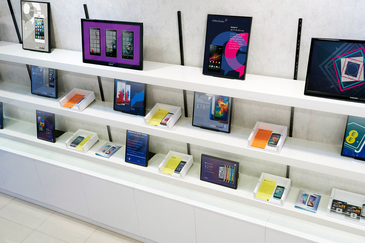 A retail display shelf showcasing various smartphones, tablets, and digital devices against a light gray wall.