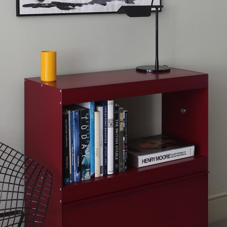 Red bookshelf with books and a yellow vase against a gray wall.
