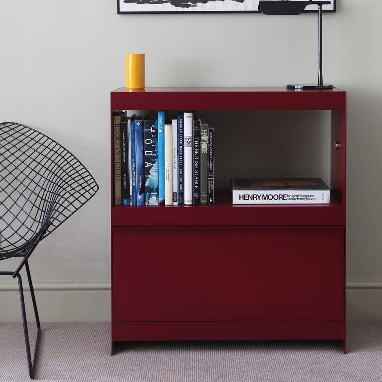 Deep red aluminium modular shelving unit with books and black light on top